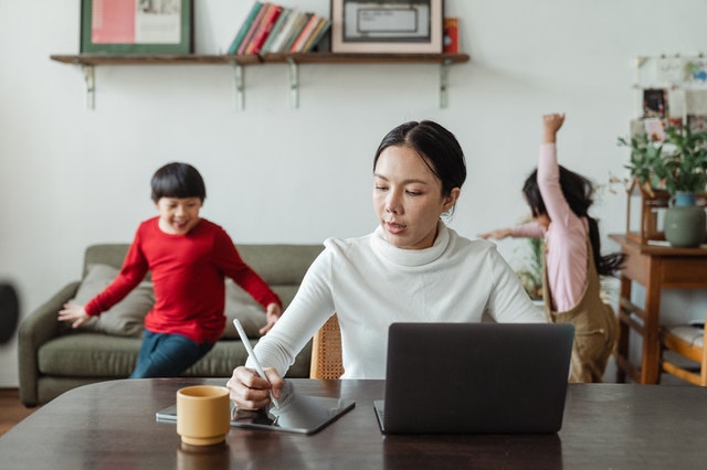 woman-working-at-home-on-laptop-at-desk-with-child-sitting-behind-on-couch